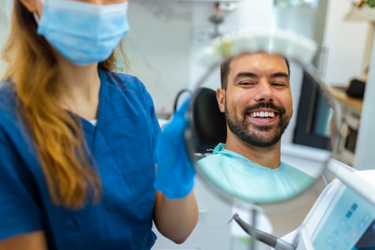 Female dentist helping patient see smile with mirror in modern dental clinic