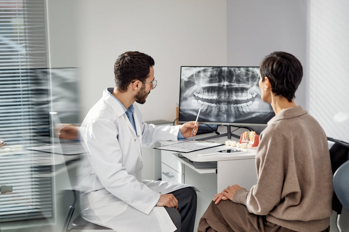 Dentist explaining dental x-ray results on monitor to patient in modern dental office